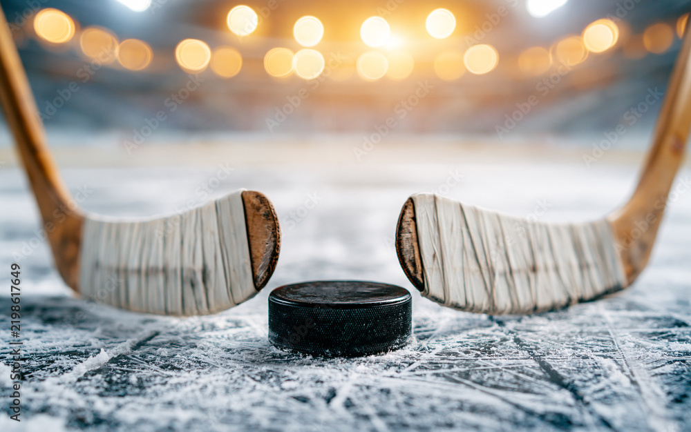 Obraz premium Two hockey sticks and puck on ice rink in stadium