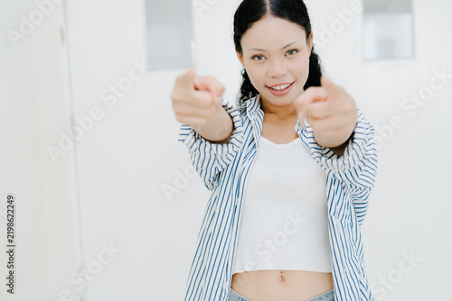 Cheerful young woman pointing forward with confident expression, feeling empowered and energetic while posing against white background