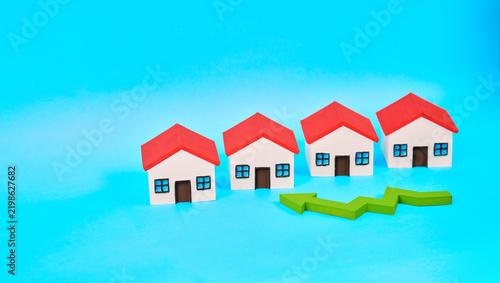 Фотография Four miniature houses next to an upward-pointing arrow represent the rise in property values