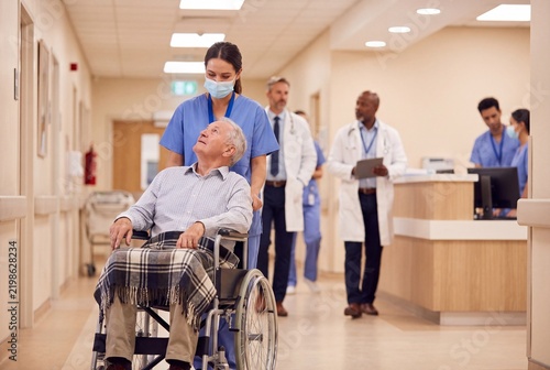 Nurse assists elderly man in wheelchair in hospital hallway