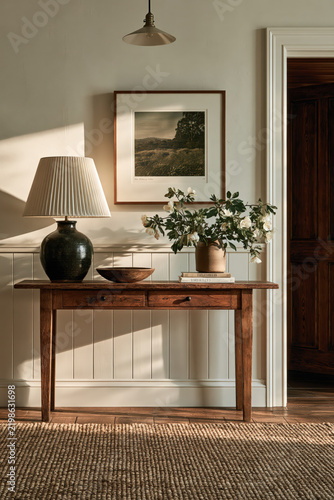 Warm hallway console table with lamp, artwork, plant, and sunlight