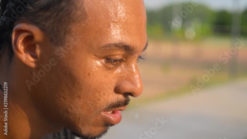 Young Black Latin man in sportswear dripping sweat breathing heavily after intense workout session in urban park daytime