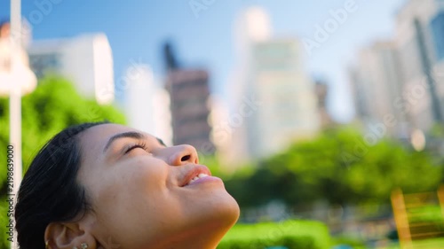 Woman, smiling and looking up at sky with satisfaction, happiness or wellness in city outdoor. Close up, person or athlete with sunlight, gratitude and contentment after workout in park.