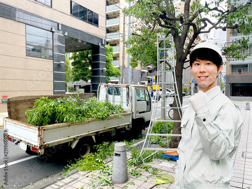 街路樹の剪定現場で微笑むアジア人男性の造園作業員
