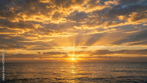 Golden Sunset Over Ocean Horizon with Dramatic Sun Rays Through Golden Clouds Reflection on Water