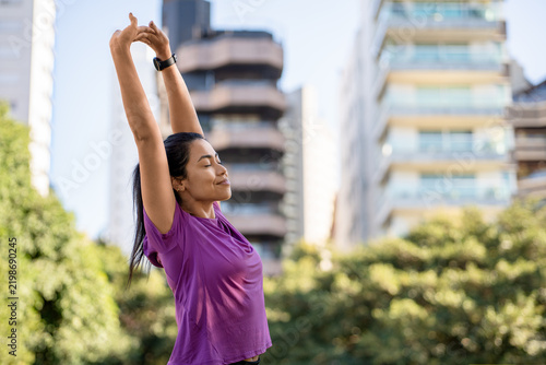 Woman, stretching and smiling in city with fitness, morning routine or wellness outdoor. Athlete or person with arms overhead, smart watch and workout warm up in park