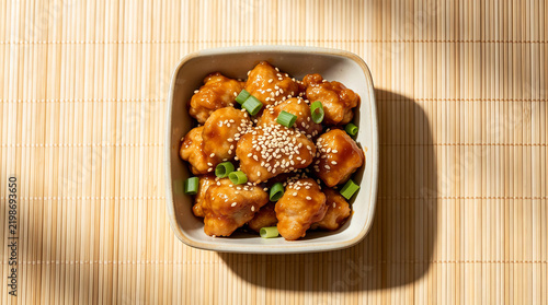 Flat lay view of sesame chicken with spring onion garnish served on bamboo mat, chinese savory meal