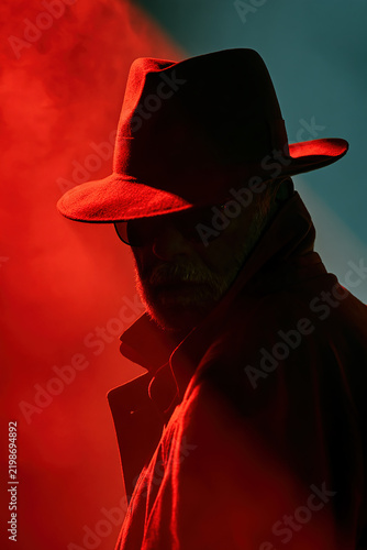 Film noir style man in a fedora hat silhouetted against red neon lights.