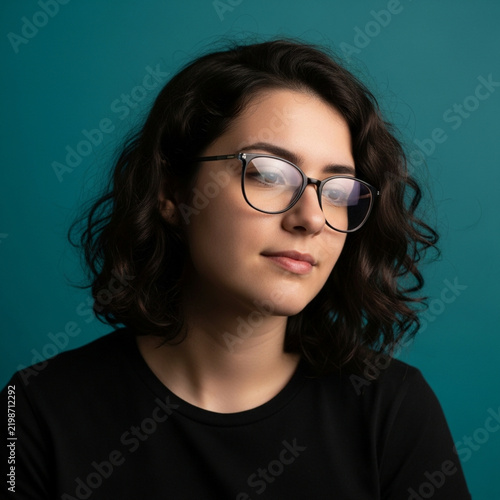 Young Woman Wearing Glasses and Black T Shirt Against Teal Background