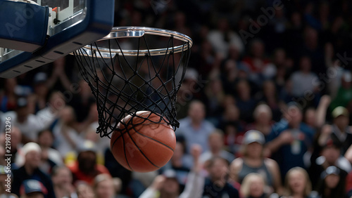 Basketball ball swishing through hoop net during competitive game in indoor arena