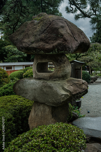 Photography Traditional Japanese stone lantern surrounded by green shrubs at Gotokuji Temple