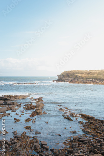 Sunlit coastal rock formations and tidal pools across Collywell Bay, Northumberland, captured during bright August 2026 shoreline conditions