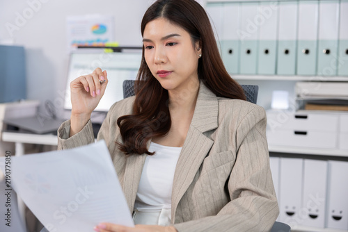 Professional woman reviewing document in modern office with focused expression and organized workspace, business planning and administrative work concept