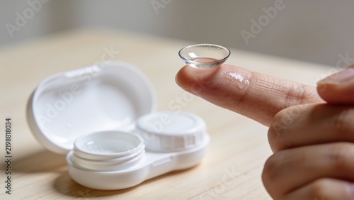 Close-up of a finger holding a clear contact lens next to its case