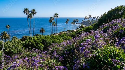 Scenic coastal view with vibrant purple flowers blooming along green hillside overlooking ocean water and tall palm trees