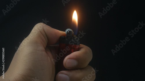 Hand holding a burning gas lighter with a small flame on a dark background