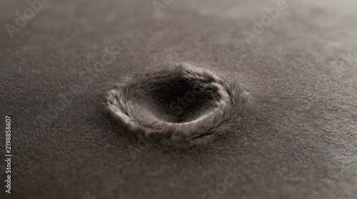 Single circular indentation on a dark grey velvet fabric surface with soft side lighting