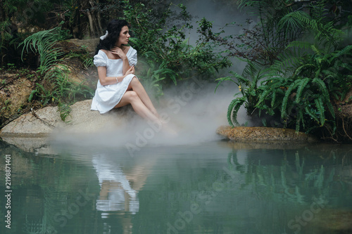 A princess or fairy in a mystical garden by the lake surrounded by trees and fog.