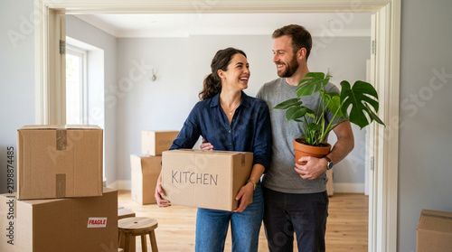 Couple moving into new home, carrying boxes and plant, happy smiling