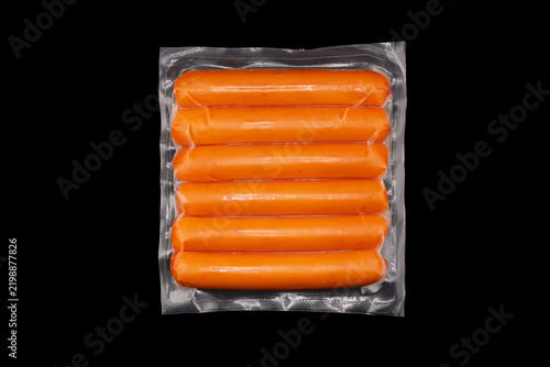 Sausages in vacuum plastic packaging isolated on black background. Vacuum transparent packaging with fresh sausages. A pack of sausages in a vacuum isolated.