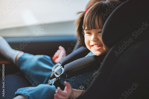 Fotografie Happy toddler girl safely secured in child car seat with safety harness inside vehicle, smiling during family journey, road travel, transportation