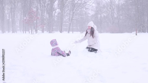 Child outdoor winter. Toddler sitting and playing in snow with mother. Family bonding concept.