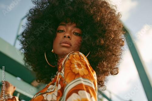 Young black woman showcasing 1970s fashion style with a voluminous afro hair and hoop earrings