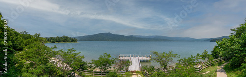 Panoramic view of Lake Akan in Akankohan, Hokkaido, Japan, surrounded by forested mountains and a scenic lakeside walking trail.