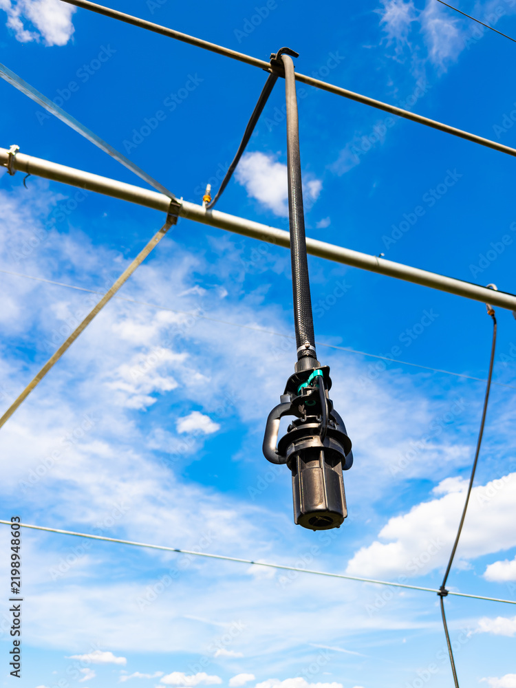 Obraz premium Hanging irrigation system on a sunny day. A hanging irrigation system is installed from pipes in the sky. The blue sky has clouds in the background.