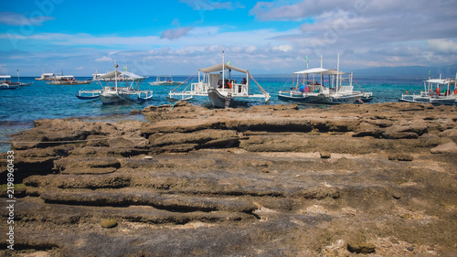 Traditional Filipino outrigger boats moored on the rocky coastline with blue water and cloudy sky overhead in Apo Island, tropical summer destination in Dauin Philippines