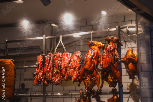 Row of hanging roast goose (siu ngo), roast duck (siu ngaap) and pork barbecue (Char siu) under warm lights at a Siu mei shop, showcasing the authentic local Cantonese food and culture. Hong Kong