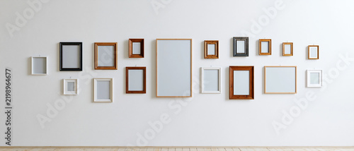 An arrangement of various empty picture frames displayed on a stark white wall, showcasing different sizes and materials in a visually appealing composition