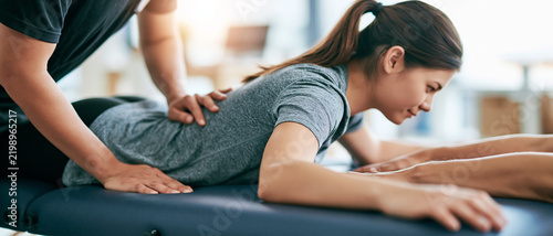 A physical therapist performing a spinal adjustment on a female patient lying face down on a massage table, providing relief and rehabilitation