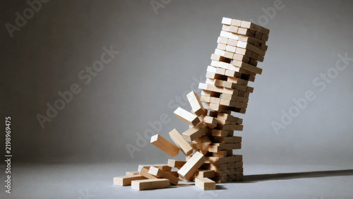 Unstable tower of wooden blocks collapsing against a neutral background, representing business risk, failure, instability, crisis, uncertainty, and financial collapse