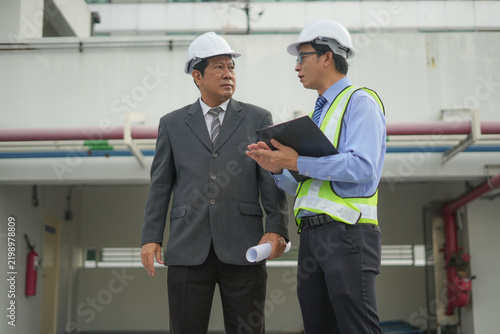 Engineer manager factory safety helmet inspection clipboard meeting at industrial plant, two male professionals discuss maintenance plan, teamwork and compliance during site audit
