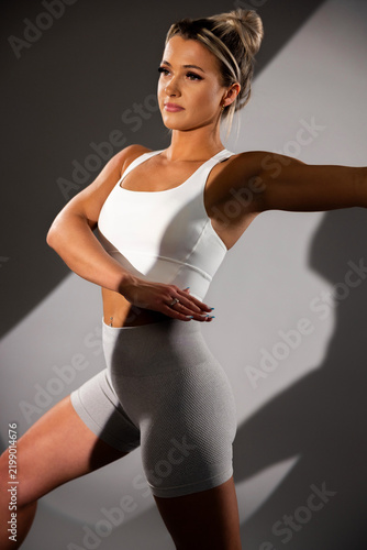 Fit woman in white sports bra and gray leggings posing in studio with dramatic lighting