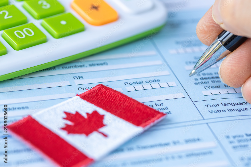 Obraz premium Tax return and application for benefits. Filing taxes in Canada. Canadian flag and person with a calculator filling out a tax form. Close up