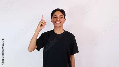 Foto Confident young Asian man smiling at the camera while raising his index finger to indicate number one or an idea against a white background