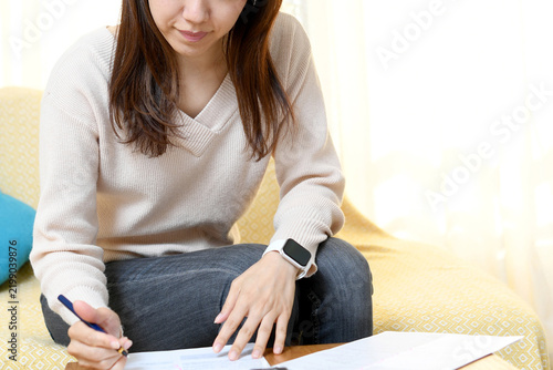 自宅のリビングで書類を書くアジア人の女性
