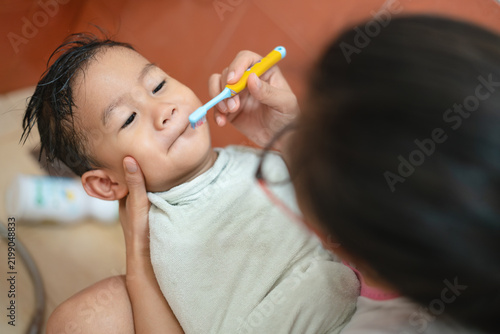 Mother brushing toddler teeth with toothbrush during bath time in Thailand