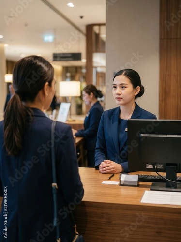Asian receptionist assisting a customer at a hotel front desk counter in a lobby
