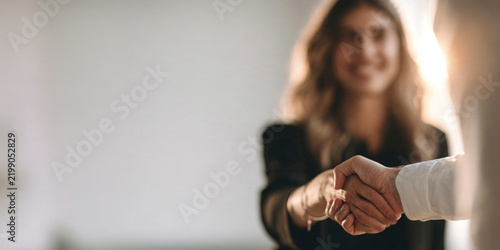 A smiling woman in a black blazer shaking hands with a business partner.