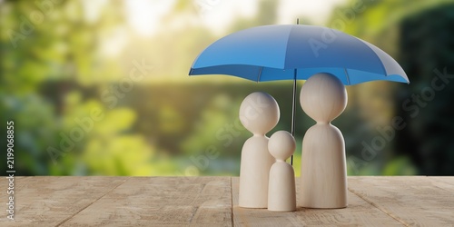 Abstract wood figure family protected by blue umbrella on wooden table over green garden background, family insurance or protection concept with copy space
