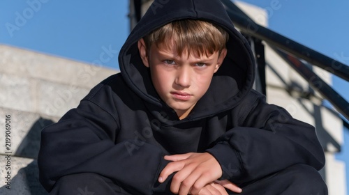 Young boy wearing black hoodie sitting on stairs looking serious