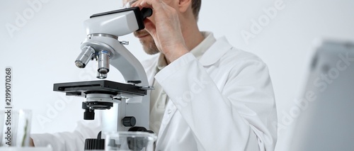 Obraz na plátne Scientist in lab coat and safety glasses looking through a microscope, performin