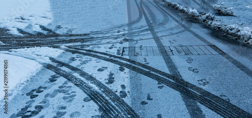 Foto Car tire marks and shoe prints on icy slippery street during winter and footprin
