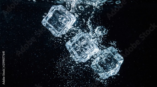 Clear ice cubes falling into fresh water creating bubbles and splashes against a dark black background