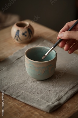 Crafting a Small Pottery Cup With a Paintbrush on a Wooden Table