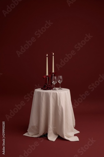 Dining Table Setup With Candles and Glasses on White Cloth Against a Brown Ba...