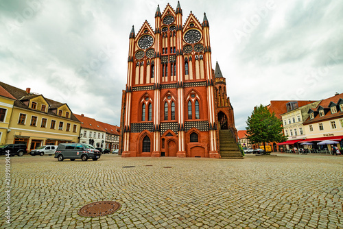 Historic Gothic brick town hall with ornate facade and decorative windows on a large cobblestone market square, photographed in landscape format.